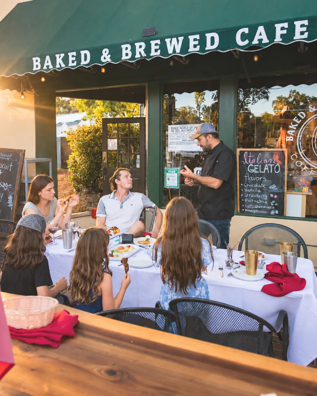 Family dining together on the patio at Baked & Brewed's Auburn storefront during golden hour